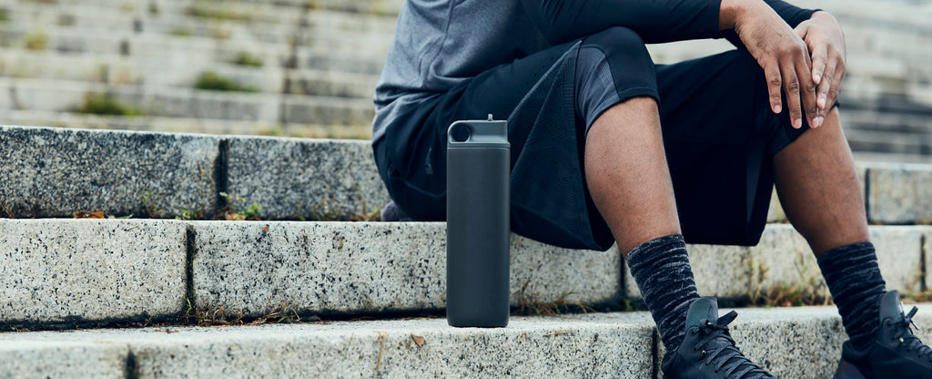 A man resting on stone steps after exercise, with a grey KINTO Active Tumbler beside him