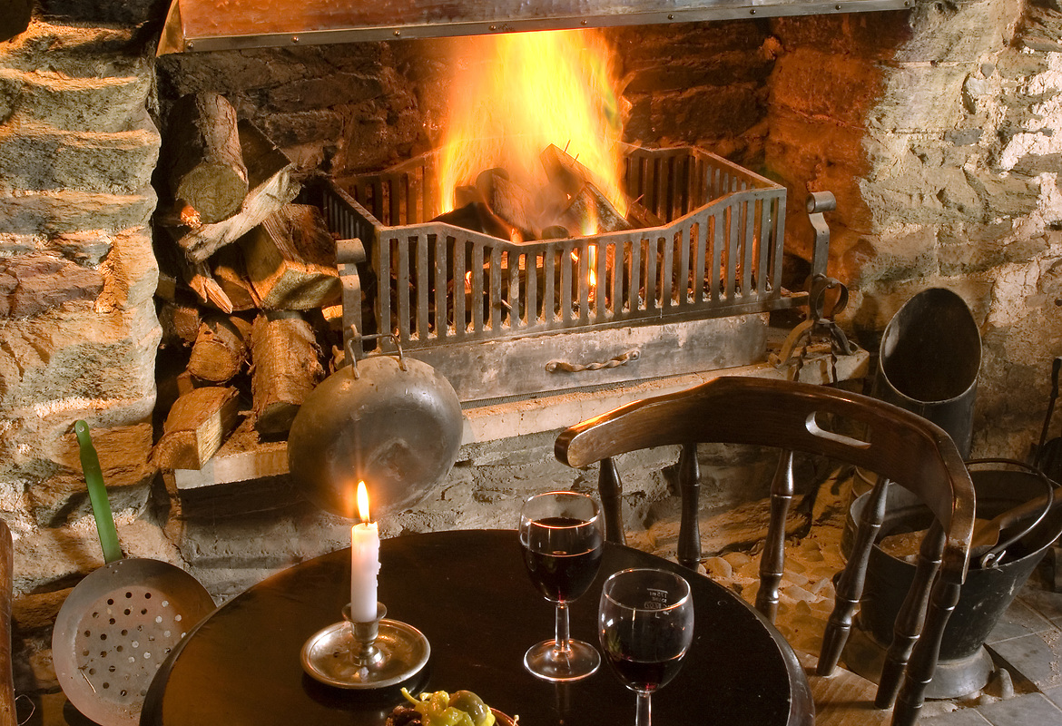 Wine glasses beside a glowing fireplace at The Pilchard Inn