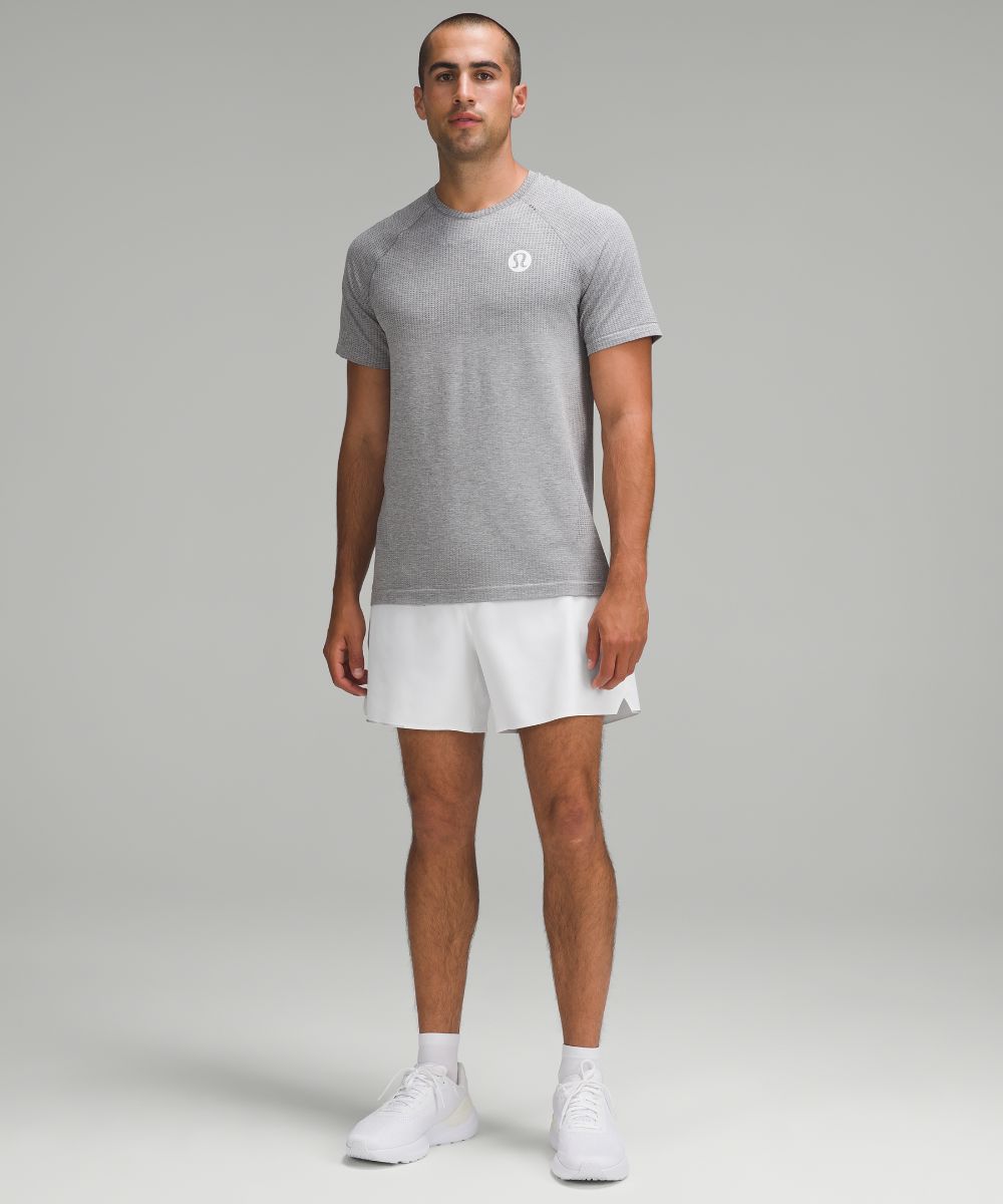 Man wearing white lululemon Surge six-inch lined shorts and a grey T-shirt; full face and body in original brand photography