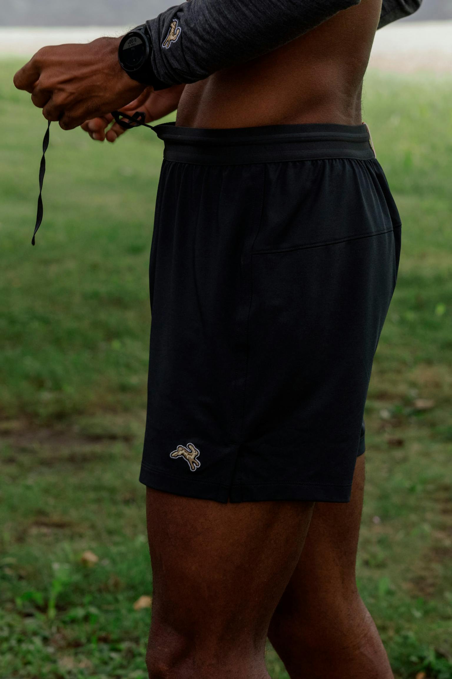 Man wearing black Tracksmith Session shorts, adjusting the waistband in original brand photography