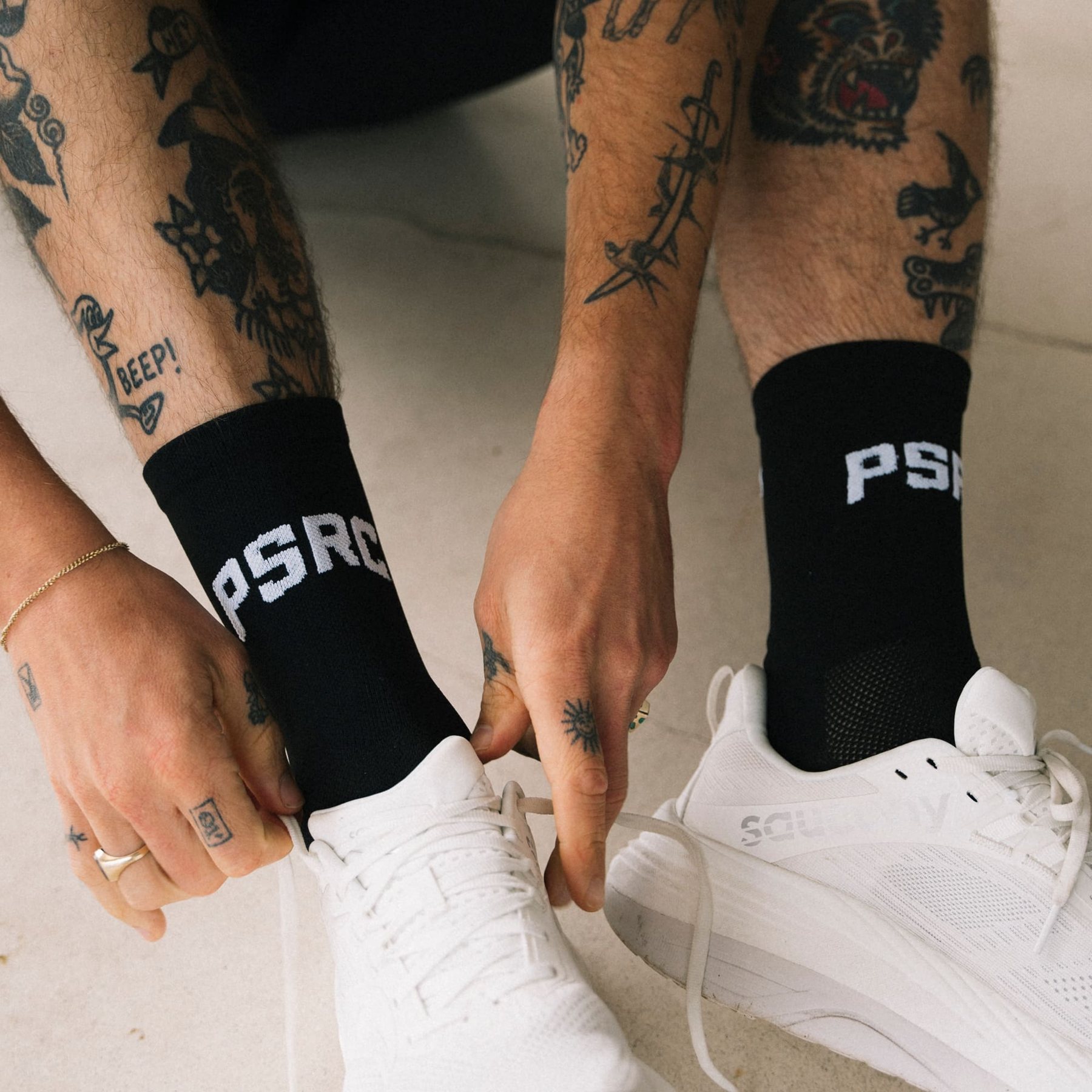 Hands tightening the laces of white trainers, with black Puresport PSRC socks visible